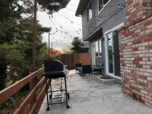 A patio with bbq and chairs on the side.