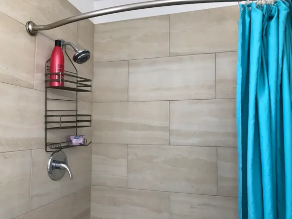 A shower with a blue curtain and a red bottle