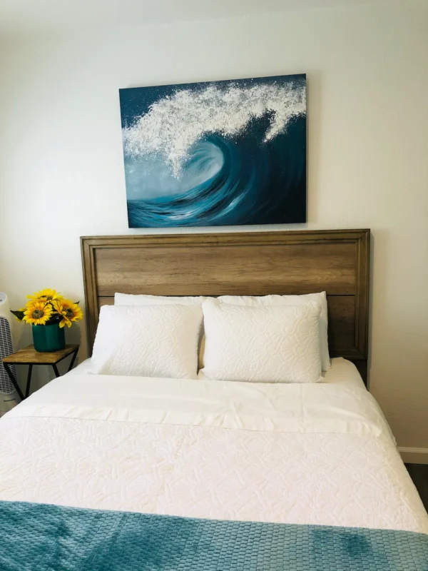 A bed with white sheets and pillows in front of a painting.