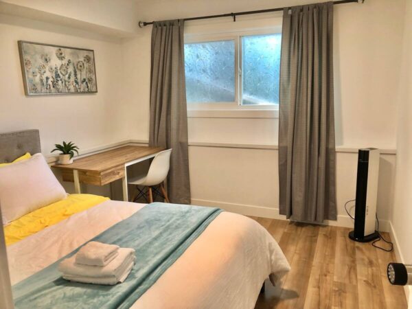 A bedroom with a bed, desk and window.