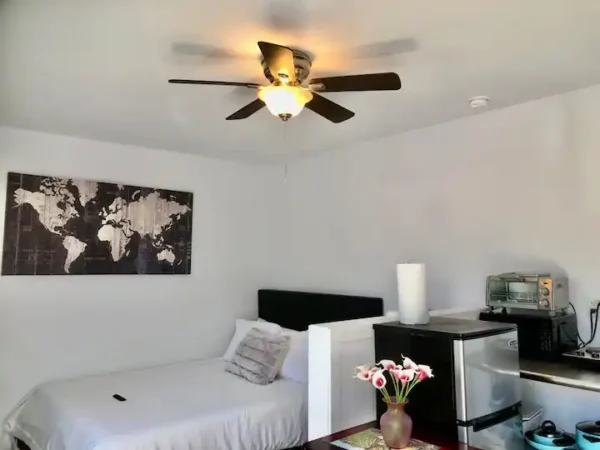 A bedroom with a bed, desk and ceiling fan.