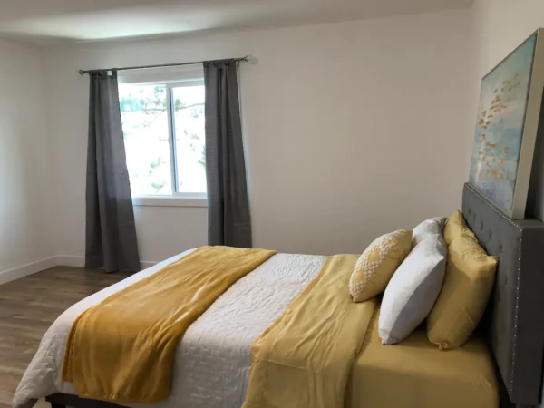 A bedroom with yellow and white bedding, two windows.