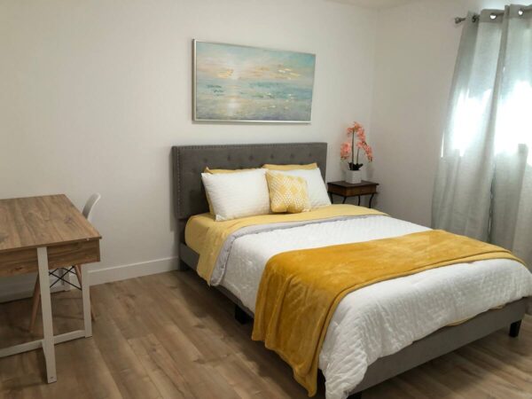 A bedroom with a bed, desk and painting on the wall.