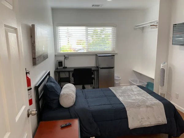 A bedroom with a bed, desk and window.