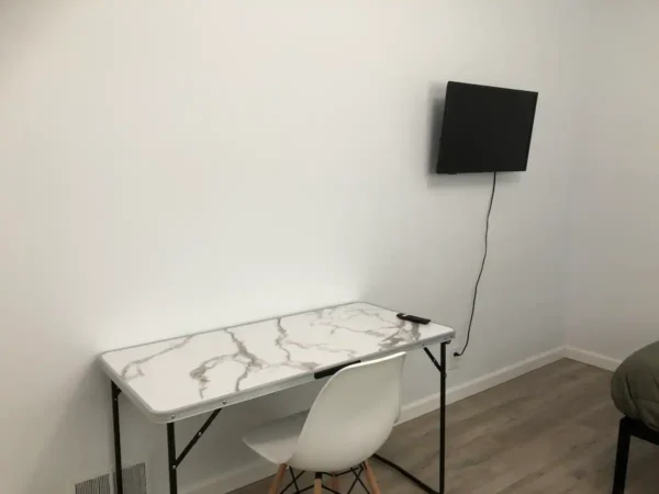 A white chair and table with a television on the wall.