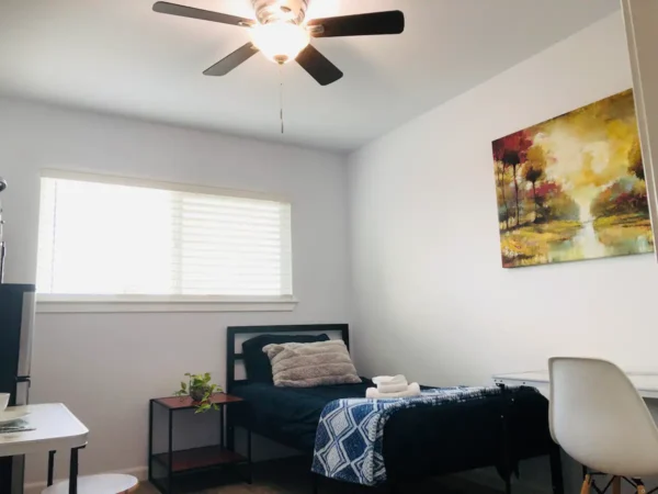 A bedroom with a bed, table and ceiling fan.