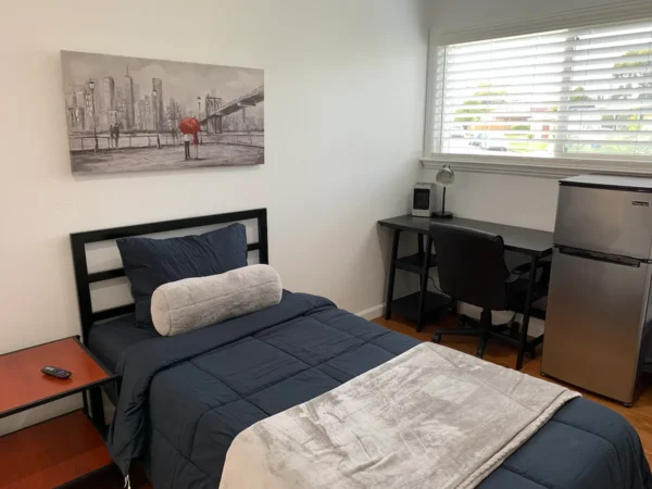 A bedroom with a bed, desk and window.