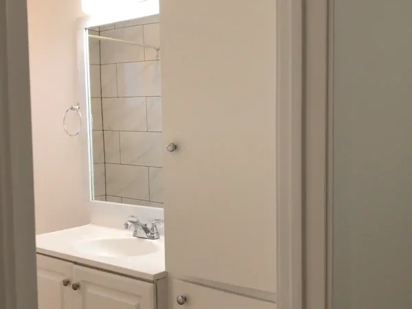 A bathroom with white cabinets and a mirror.