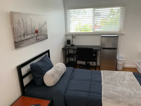 A bedroom with a bed, desk and small refrigerator.