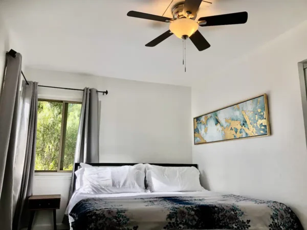 A bedroom with a bed, ceiling fan and window.