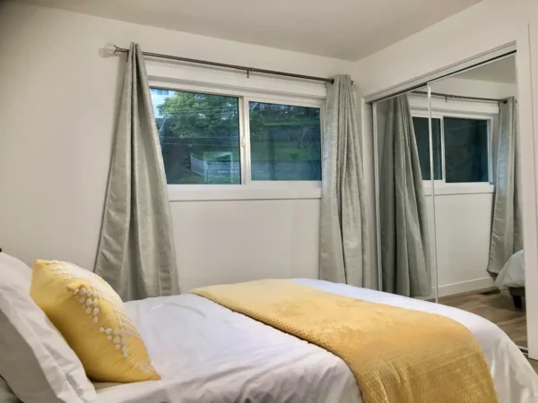 A bedroom with yellow and white bedding, two windows.