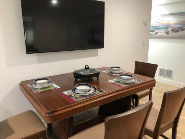 A dining room table with four chairs and a television.