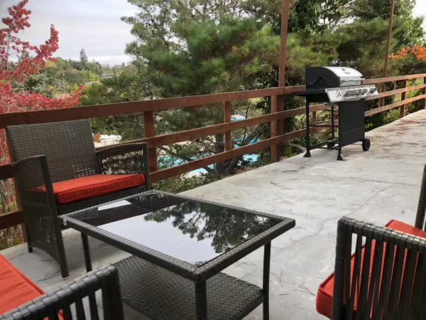 A patio with tables and chairs, grill and trees.