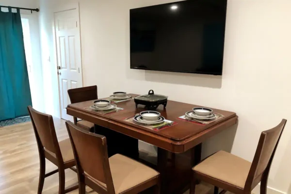 A dining room table with four chairs and a television.