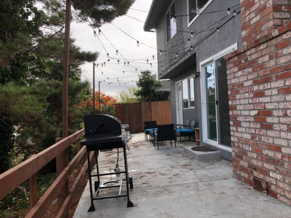 A patio with a grill and chairs on the side.