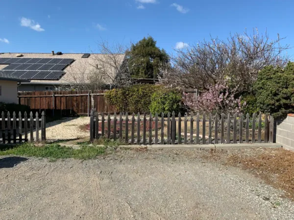 A fence that is near some trees and a house.