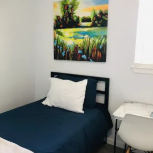 A bedroom with a bed, chair and painting on the wall.