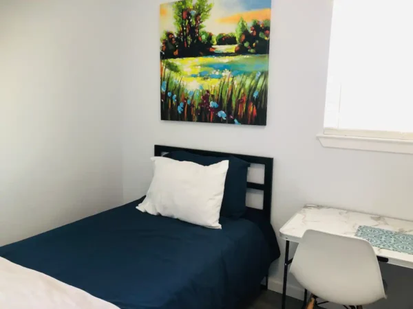 A bedroom with a bed, chair and painting on the wall.