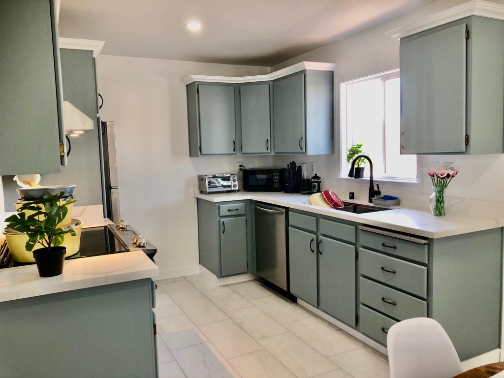 A kitchen with green cabinets and white tile floors.