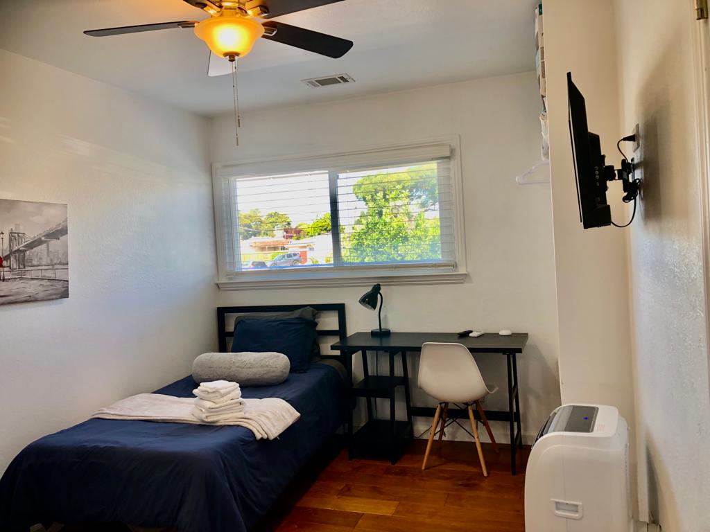 A bedroom with a bed, desk and air conditioner.